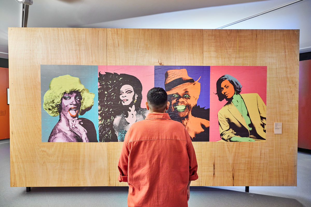 Imagem mostra um homem de costas olhando para obras do Museu da Diversidade Sexual.