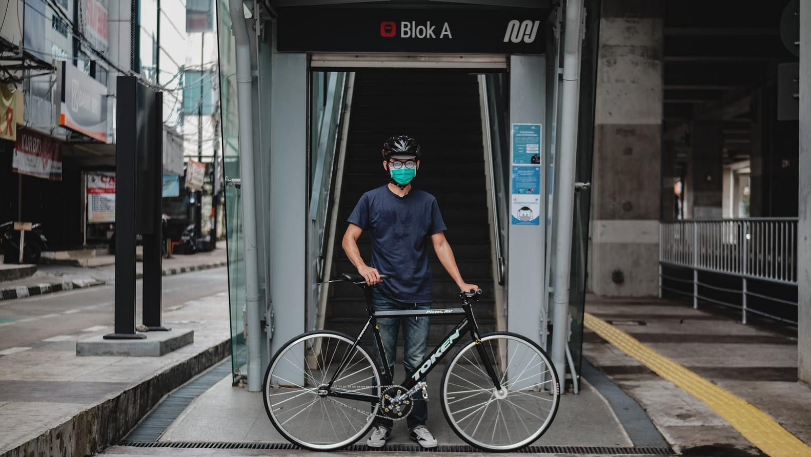 ciclista com máscara na frente da entrada do metrô